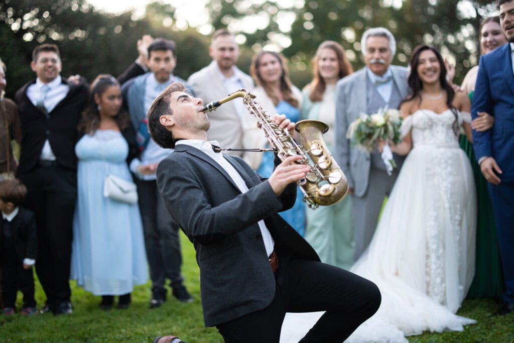 Group photo of bride, groom and friends in the gardens of Villa Wenkenhof, Switzerland. Saxophon player