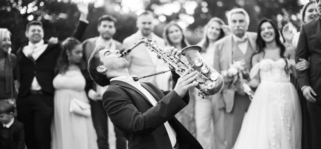 Group photo of bride, groom and friends in the gardens of Villa Wenkenhof, Switzerland. Saxophon player