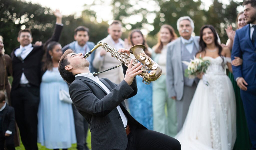 Group photo of bride, groom and friends in the gardens of Villa Wenkenhof, Switzerland. Saxophon player
