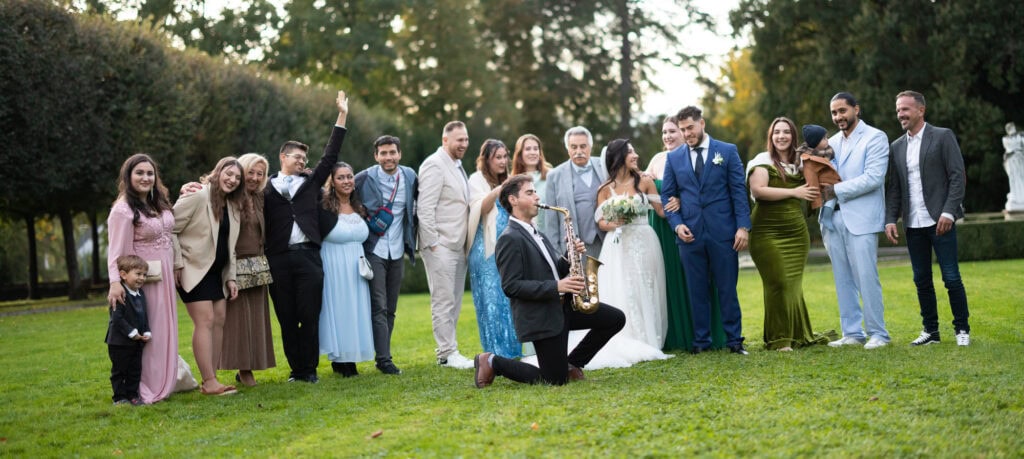 Group photo of bride, groom and friends in the gardens of Villa Wenkenhof, Switzerland. Saxophon player