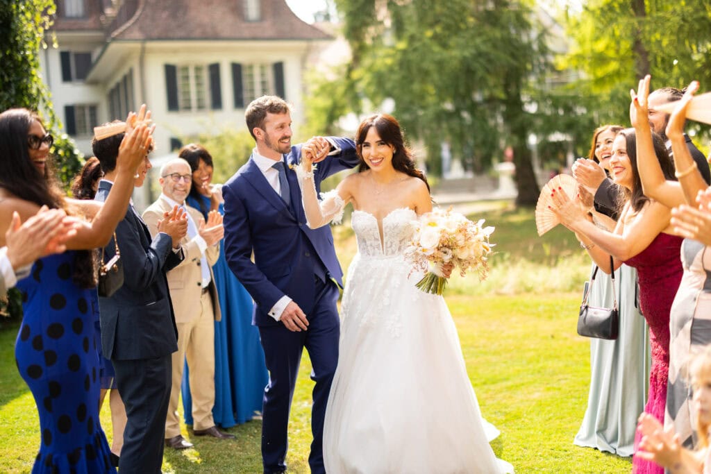 Guests forming a celebratory aisle (Spalier) for the bride and groom after the ceremony during their wedding at Schloss Hünigen in Bern