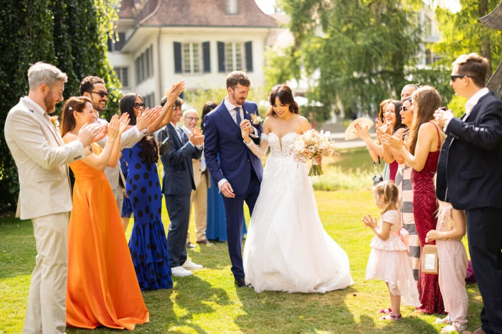 Guests forming a celebratory aisle (Spalier) for the bride and groom after the ceremony during their wedding at Schloss Hünigen in Bern