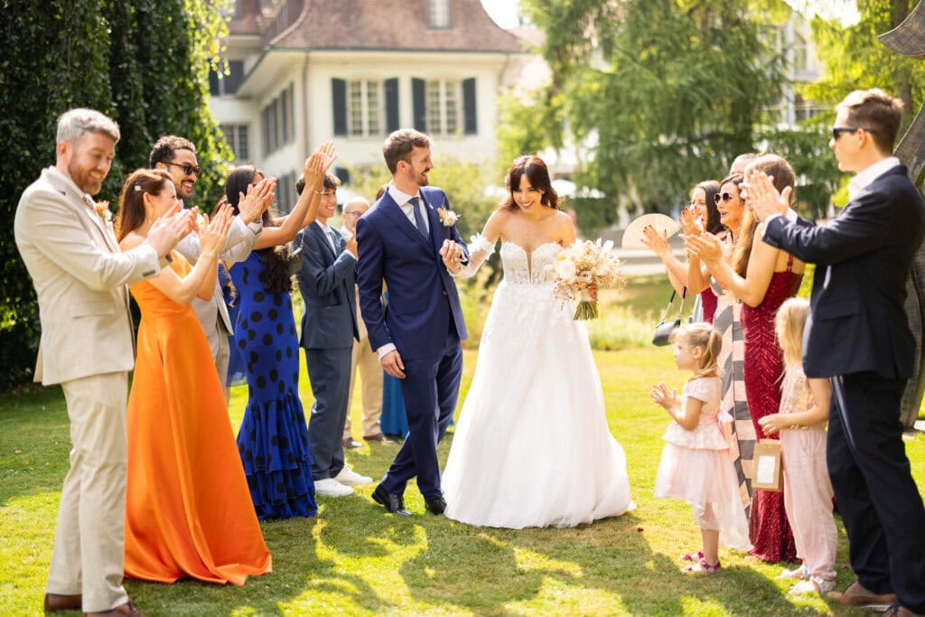 Guests forming a celebratory aisle (Spalier) for the bride and groom after the ceremony during their wedding at Schloss Hünigen in Bern