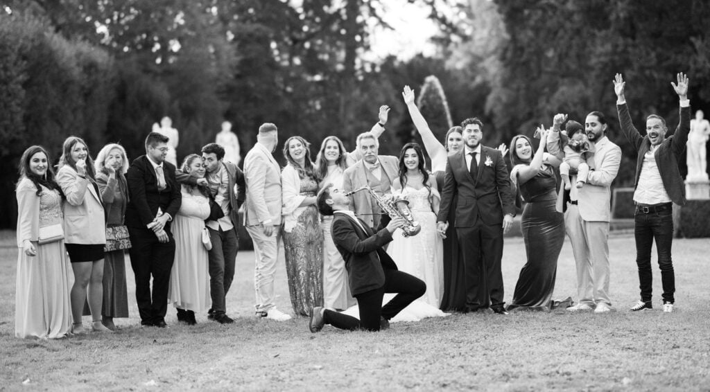 Group photo of bride, groom and friends in the gardens of Villa Wenkenhof, Switzerland. Saxophon player