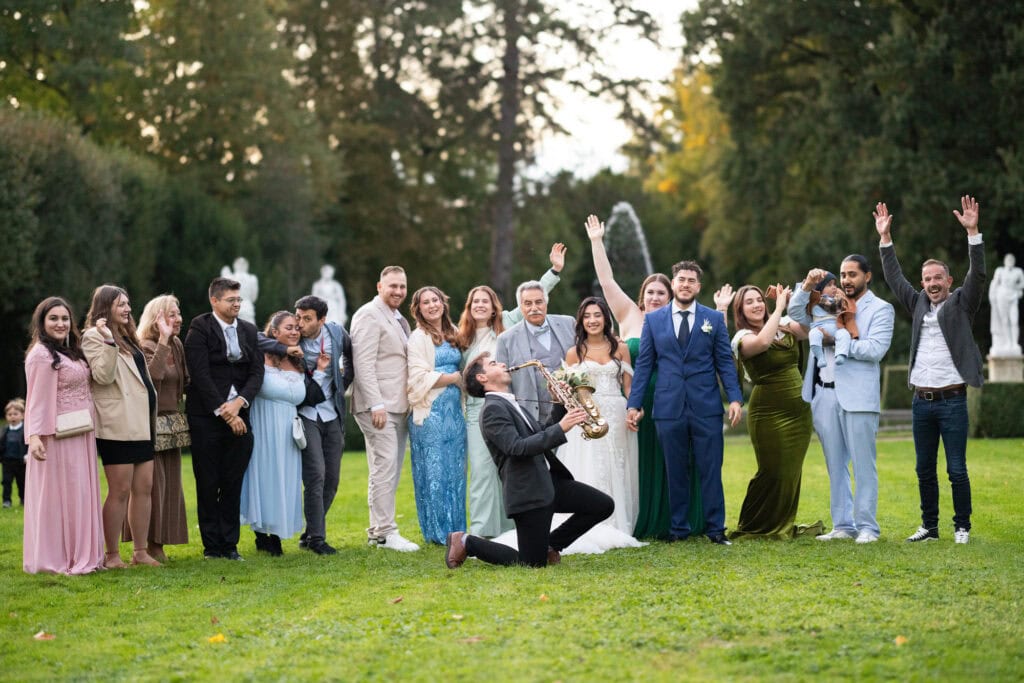 Group photo of bride, groom and friends in the gardens of Villa Wenkenhof, Switzerland. Saxophon player